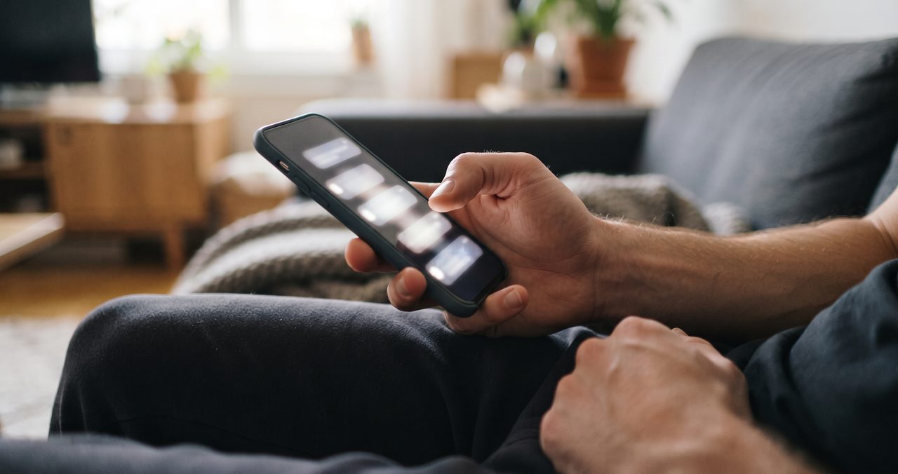 リビングのソファで、通知が積み重なって表示されたスマートフォンを手に持ち画面を見つめている手元のクローズアップ